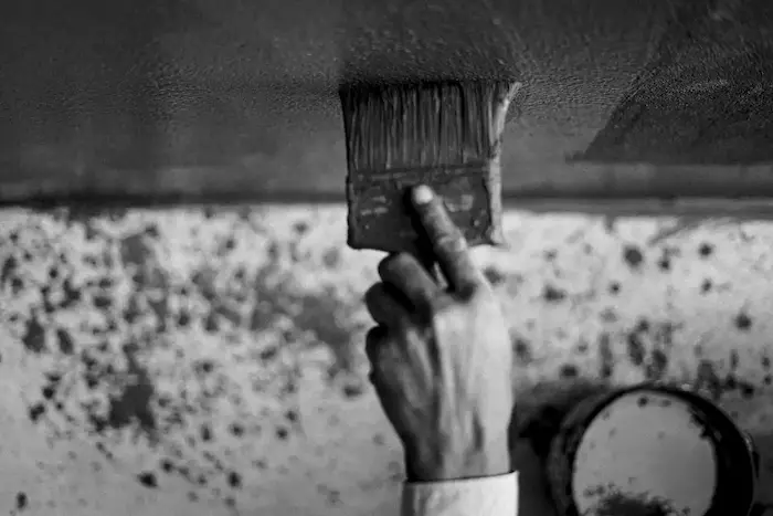 Une main tenant un pinceau en train de peindre un mur, l’image est en noir et blanc.