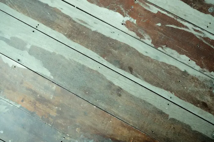 Un sol en bois usé avec des traces de peinture blanche et des taches sombres, montrant des signes d'usure et de décoloration.