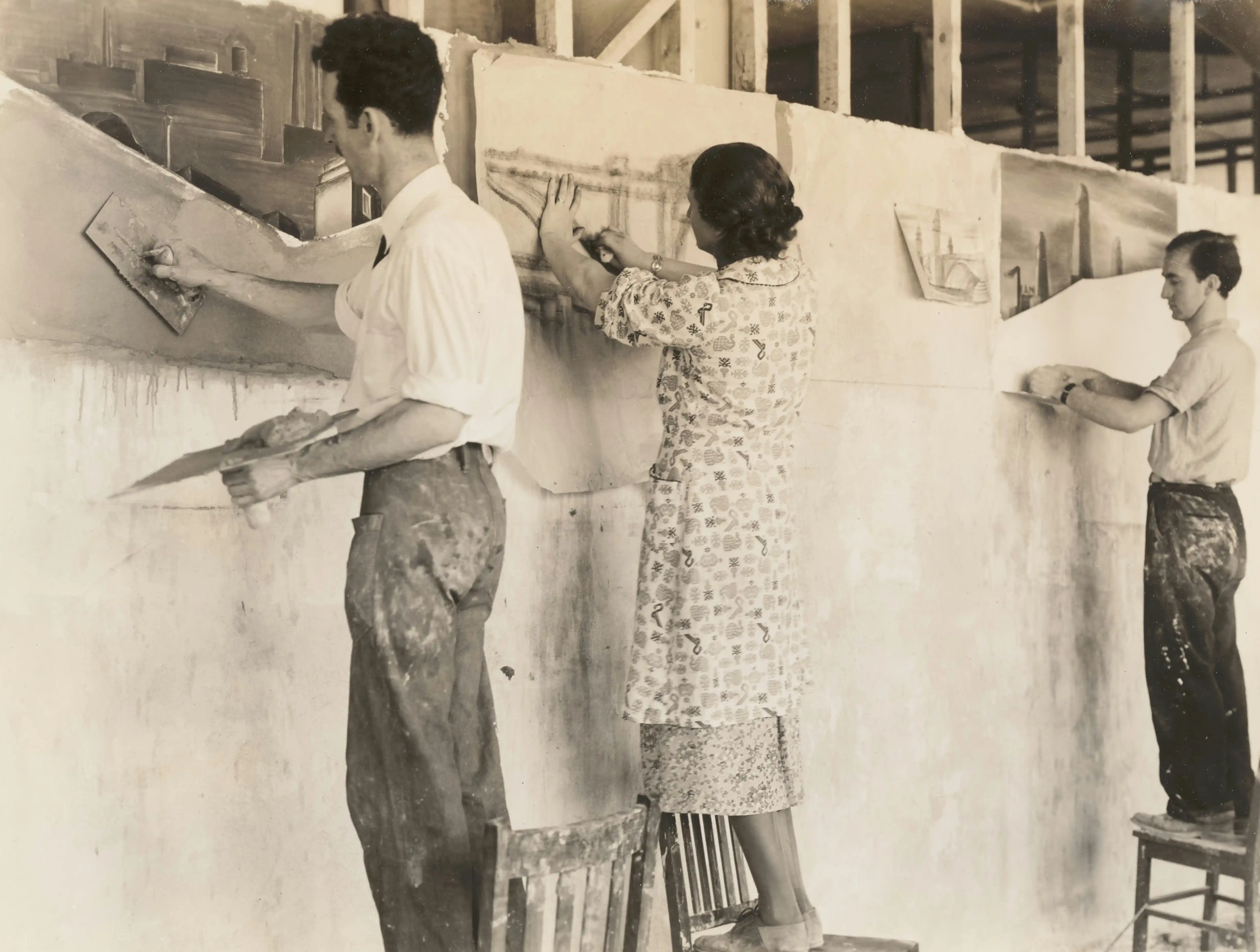 Trois personnes peignant une fresque murale. Deux hommes et une femme, vêtus de vêtements de travail, utilisent des pinceaux